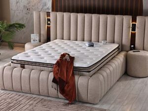 Noble boxspring in taupe suèdelook met breed geribbeld hoofdbord en geïntegreerde leeslampen